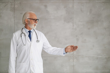 Senior doctor in a white coat gestures confidently in a modern clinic setting during a check-up consultation