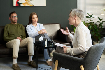 Obraz premium Middle aged woman psychologist conducting therapy session with man and woman sitting on couch listening attentively