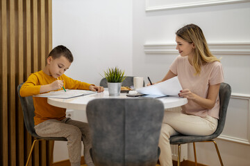 Mother helps her son with homework at a cozy table in a bright indoor space during the afternoon