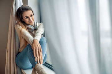 Woman sitting by the window smiling and enjoying music while wrapped in soft natural light at home