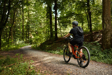 Naklejka premium A man rides a bicycle through a forested area using a navigator.