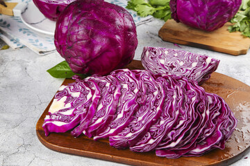 Obraz premium Fresh Purple Cabbage Slices on Wooden Cutting Board with Leafy Vegetables in Kitchen