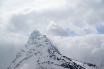 High snowy mountains in fog and cloudy sky at winter