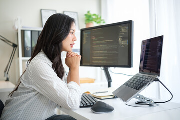 Concentrated woman coder analyzing software code on dual monitors in a modern workspace.