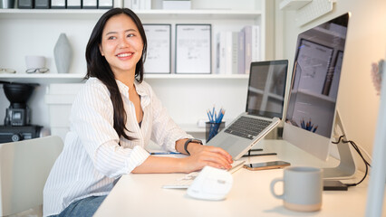 Cheerful female software developer working at a clean desk with dual screens.