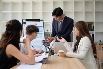 Businessman uses a calculator to explain financial figures to team members.