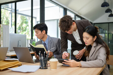 Group of young professionals collaborating on a project using digital devices in a modern office.