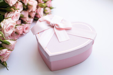 A bouquet of pink roses and a heart-shaped gift box on white background.