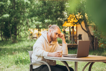 Fototapeta premium Man using laptop in the morning on a sunny day away from the city on a campsite.