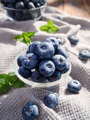 Fresh Yunnan Mountain Blueberries with Mint in Glass Bowl on Rustic Linen Background