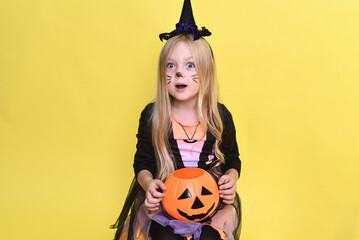 Cute little girl in a witch costume is sitting on a big pumpkin for Halloween.