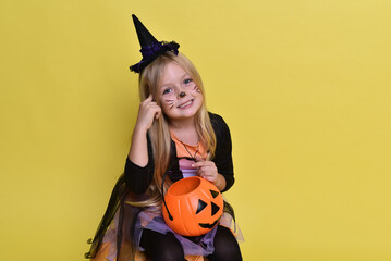 Cute little girl in a witch costume is sitting on a big pumpkin for Halloween.