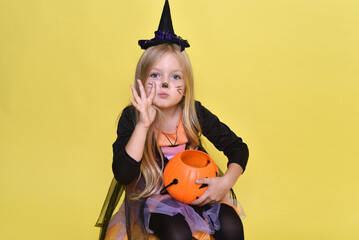 Cute little girl in a witch costume is sitting on a big pumpkin for Halloween.