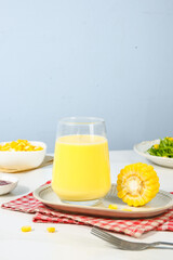 Fresh corn juice in glass with corn cob and kernels on white table - healthy vegetable drink concept