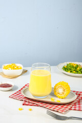 Fresh Corn Juice in Glass with Corn Kernels and Healthy Salad on White Table