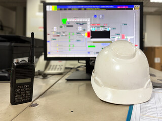 Workplace safety equipment and industrial control monitor at plant facility depicting communication walkie-talkie radio and protective hardhat for workers safety management at construction site