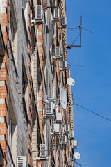 The wall of a multi-storey apartment building with numerous air conditioners and antennas. Soft focus