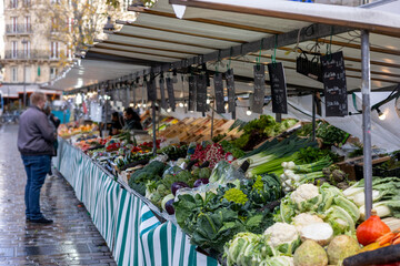 Fototapeta premium Fresh vegetables, including cauliflower, leeks, artichokes, radishes, kale, romanesco cabbage and cabbage, are for sale at a street market in Paris, France. A vendor is in the background.