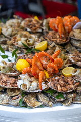 A large seafood platter with a variety of fresh seafood, including oysters, whelks, shrimp, prawns, and scallops, is a presentation of the market's assortment and a tasting set in Paris, France.