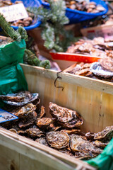 Fresh oysters are for sale in a wooden crate at a street seafood market in Paris, France. One oyster is open, revealing the meat inside.