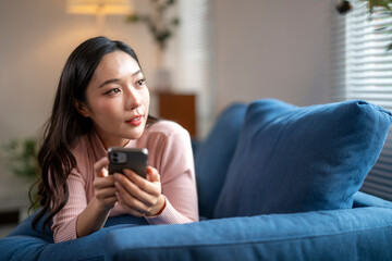 Young woman relaxing on sofa using smartphone at home