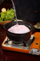 Fresh whole raw chicken being washed in pot on gas stove burner for cooking preparation