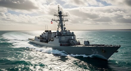 A gray warship cruises through turquoise ocean waters leaving a white wake under a cloudy sky
