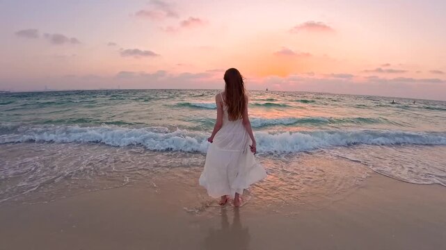 Woman in long white dress walking towards the sea sunset on the beach seashore, real time. Freedom and joy of movement. With the sound of the surf and the wind