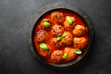 Meatballs in tomato sauce in iron plate on black background.