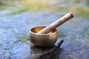 Tibetan singing bowl with mallet on stone in river, closeup