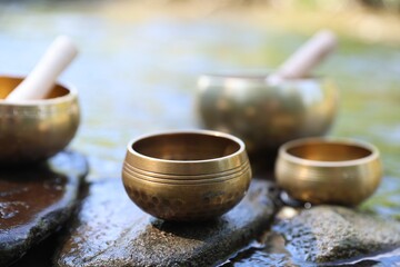 Tibetan singing bowls with mallets on stones in river, closeup