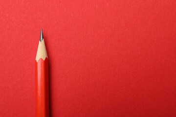 One sharp graphite pencil on red background, top view. Space for text