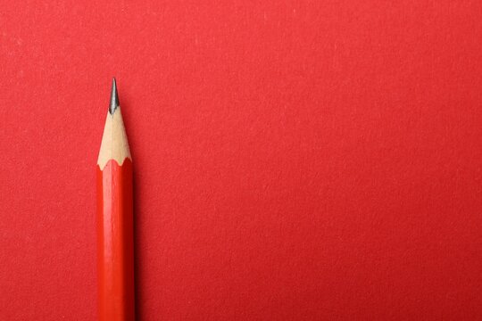 One sharp graphite pencil on red background, top view. Space for text