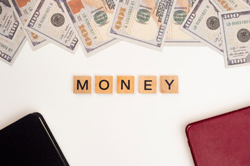 Wooden block tiles with the letters "Money" on a white background. The word "Money" is written on a wooden block or wooden cube with money, books, and credit cards on an office desk.