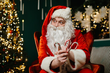 Santa claus holding candy canes near christmas tree