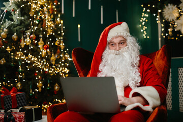 Santa claus using laptop near christmas tree and gifts