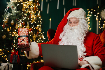 Santa claus showing christmas gift during video call on laptop