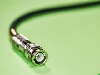 BNC connector at the end of a black cable - A detailed close-up of a shiny BNC connector attached to a black coaxial cable, isolated on a green background.