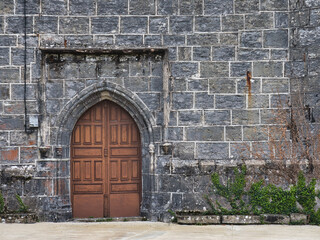 Medieval arched wooden door in an old stone wall - A full-frame shot of an ancient stone wall with a prominent, arched wooden door in a medieval style.