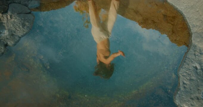 Reflection of woman in tidal pool with surrounding nature during contemporary dance