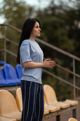 brunette girl stands in an empty stadium wearing a blue T shirt and striped pants. She celebrates her victory with a proud gesture enjoying the moment of success in a peaceful atmosphere.