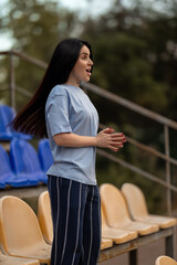 Excitement fills the air as a brunette girl in a blue T shirt cheers for her victory in an empty stadium. Her joyful expression reflects pure enthusiasm and happiness.