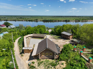 An aerial view of historical wooden buildings, including a large log cabin, on a hill overlooking...