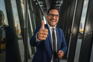 Smiling businessman showing thumbs up in front of modern office building