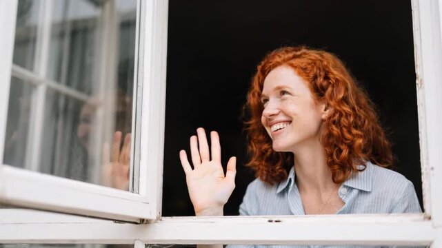 Head and shoulders view of redhead in early 30s smiling and waving at admirers from half-open window