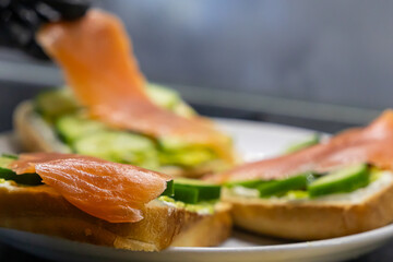 Chef's gloved hand expertly places fresh smoked salmon onto a healthy breakfast toast, topped with creamy cheese and crisp cucumber slices, for gourmet catering