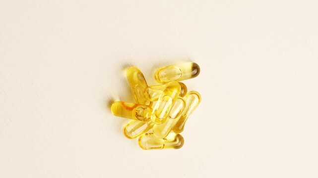 Many golden translucent omega three oil capsules stacked together on a clean white surface for a health related composition