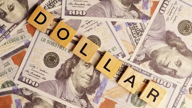 Wooden letter tiles spelling the word dollar placed on a pile of one hundred dollar bills for financial business concepts