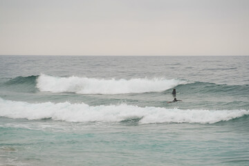 Praia Pequena do Rod&iacute;zio, Sintra, Portugal. Waves, surfers, sand, clouds. Coastal landscape, natural texture, calm atmosphere, water sports.