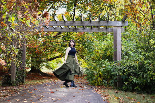 Beautiful young woman under an arbor skirt twirling at legs at a park